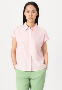Camisa de botão de manga curta, às riscas rosa e branca, com colarinho, feita de tecido leve; usada com calças verdes.