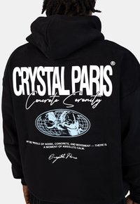 Czarna bluza z kapturem z dużą białą grafiką z tyłu, która zawiera napis "CRYSTAL PARIS", wzór globusa i slogan "Betonowa Serenity".