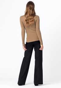 Geribbelde bruine top met lange mouwen, gecombineerd met zwarte, wijde broeken. De outfit heeft een aansluitend ontwerp en een zachte textuur.