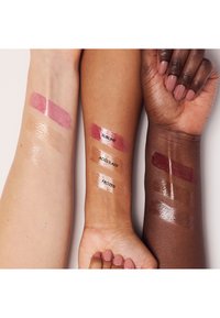 Trois bras présentent des échantillons de rouges à lèvres : des gloss roses et translucides étiquetés « Sublime », « Accolade » et « Frozen », mettant en valeur différentes teintes de peau.
