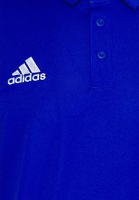 Polo en tissu bleu vif, avec un col classique, deux boutons, et un logo Adidas blanc brodé sur le côté gauche de la poitrine.