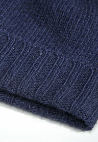 Marineblå ribbet strikket stoff med myk tekstur, med horisontale mønstre og en brettet kant. Synlige fibre for et koselig utseende.