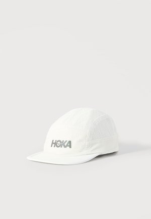 Hvid mesh løbekasket med buet skygge og et reflekterende "HOKA"-logo på frontpanelet, sat mod en ensfarvet baggrund.