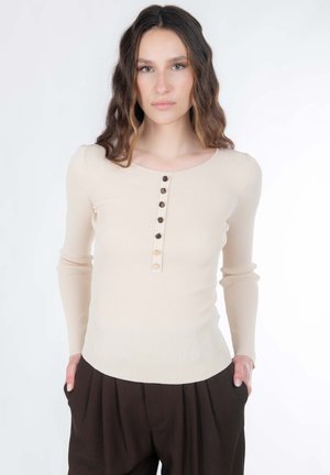 Haut beige côtelé à manches longues avec un col rond et une patte de boutonnage à six boutons. Associé à un pantalon marron foncé taille haute. Texture lisse.