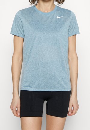 Femme portant un t-shirt Nike bleu clair à manches courtes et un short de cyclisme noir texturé, debout devant un fond blanc uni.