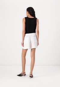 Top negro de punto sin mangas con un escote en forma de ondas, combinado con pantalones cortos blancos con cintura elástica y dos bolsillos traseros. Zapatos negros.