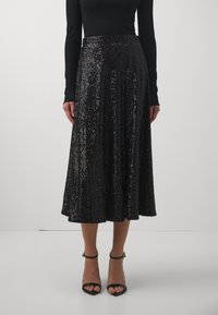 Svart paljetterad midi kjol med utställd design och elastisk midja, med en glittrande textur och parat med svarta sandaler med klack och remmar.