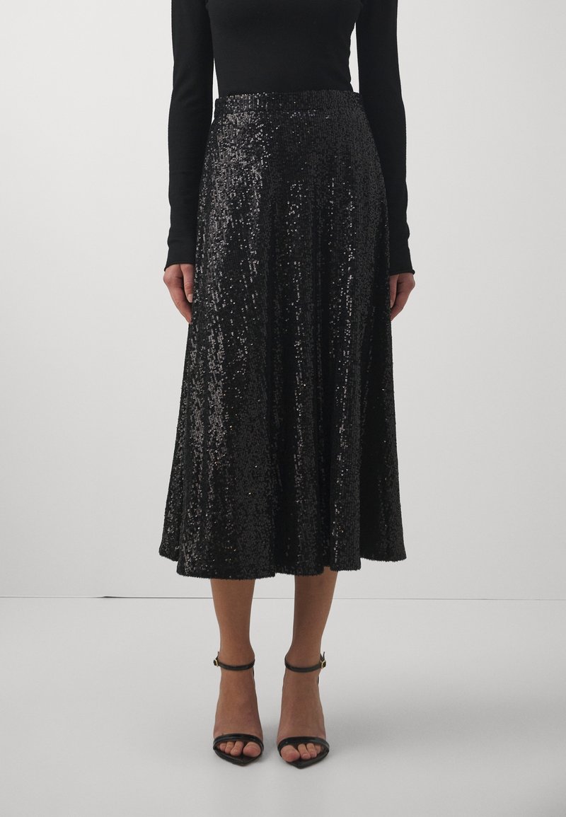 Svart paljetterad midi kjol med utställd design och elastisk midja, med en glittrande textur och parat med svarta sandaler med klack och remmar.