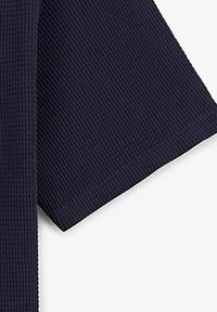 Marineblauwe ribstof met een gestructureerde oppervlakte; close-up van de rand van een mouw van een kledingstuk, met nette stiksels en een rechte snit.