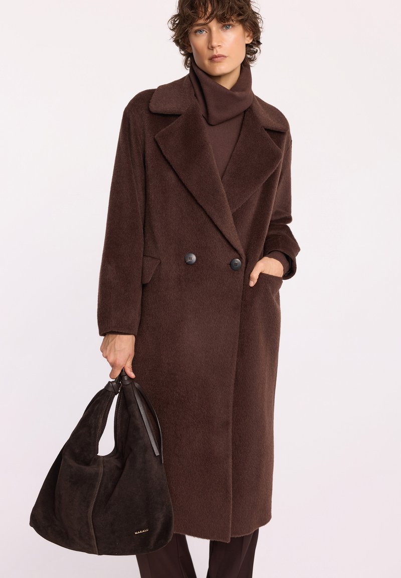 Brązowy płaszcz z wełny z podwójnym zapięciem, dużymi klapami i bocznymi kieszeniami. W połączeniu z ciemną torebką z zamszu.