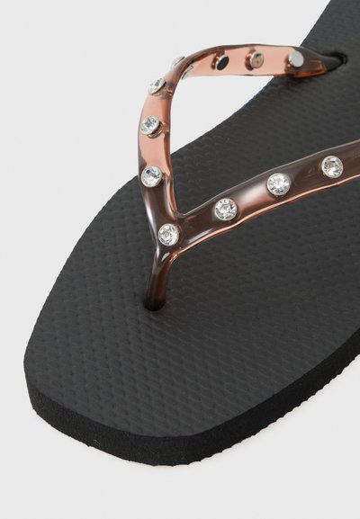 Sorte flip-flops med en teksturert såle og gjennomsiktige brune stropper dekorert med klare rhinestones.