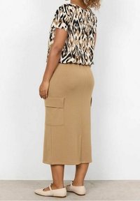 Woman wearing a beige midi skirt with side pockets, a short-sleeve animal print blouse, and beige Mary Jane flats, standing on a gray floor.