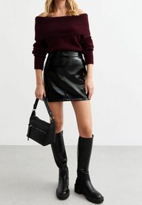 Suéter acanalado burdeos sin hombros, falda mini de piel sintética negra, botas negras hasta la rodilla y un pequeño bolso negro con cremallera.