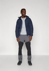 Tamsiai mėlyna pūkinė striukė su gaubtu, pilka marškinėlių ir pilkai juodos spalvos kelnės. Tvirtas juodas avalynė. Paprastas, funkcionalus dizainas, tinkamas nešioti lauke.