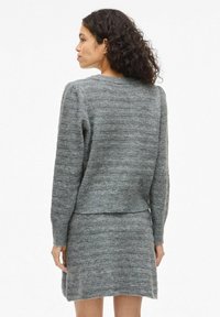 Jersey de punto gris con mangas largas y un diseño cortado, que presenta un patrón de rayas horizontales texturizadas.