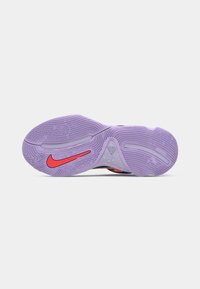 Fialová gumová podrážka tenisky s texturovanými gripovými vzory a červeným logem Nike blízko prstové části.