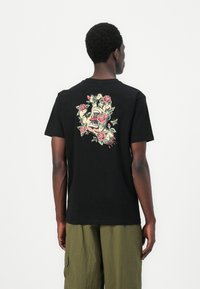 Black cotton t-shirt with short sleeves, featuring a colorful graphic design of a skull and roses on the back. Simple crew neckline.
