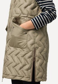 Beżowa pikowana kamizelka z zapinaną na zamek kieszenią boczną oraz kieszenią na zatrzask. Posiada wysoki kołnierz oraz gładką, połyskującą teksturę.