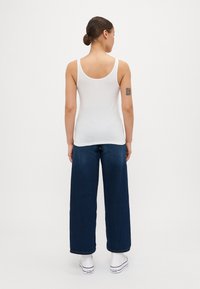 Hvit tettsittende ermeløs topp med tynne stropper, sammen med løse blå denimbukser og hvite sneakers. Rett skjæring, glatt tekstur.