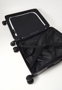 Black wheeled suitcase with a smooth exterior, featuring a zippered compartment with a white zipper and internal straps for securing items.