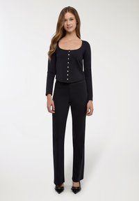 Top nero a maniche lunghe con scollo rotondo e dettagli con bottoni argentati, abbinato a pantaloni neri a gamba dritta e scarpe nere con punta appuntita.