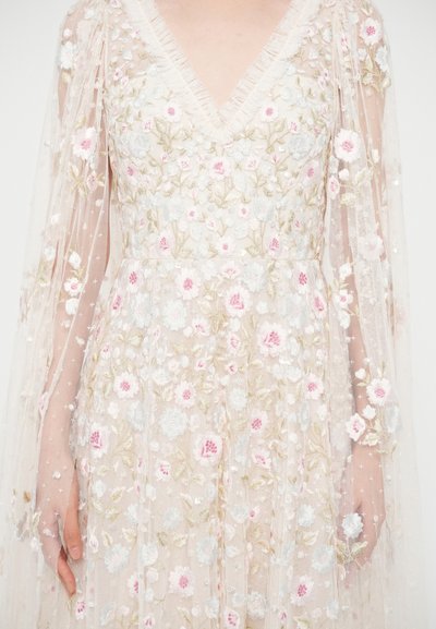 Vyšívané šaty s véčkovým výstrihom, priesvitnými dlhými rukávmi, kvetinovými vzormi v ružovej a bielej farbe a textúrovanou vrstvou. Ozdobené flitrami.