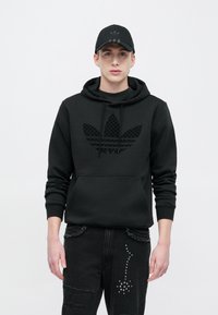 Felpa con cappuccio nera con logo Adidas nero testurizzato, tasca a marsupio, cappuccio a strati. Abbinata a jeans neri consumati con accenti argentati.