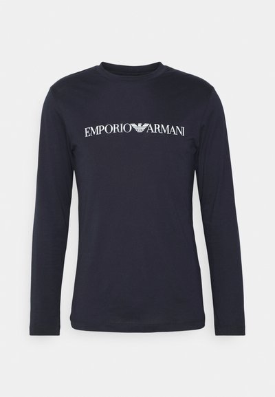 Tumesinine pikkade käistega T-särk, mis on valmistatud siledast kangast ja millel on rinnal stiliseeritud valge "EMPORIO ARMANI" logo.
