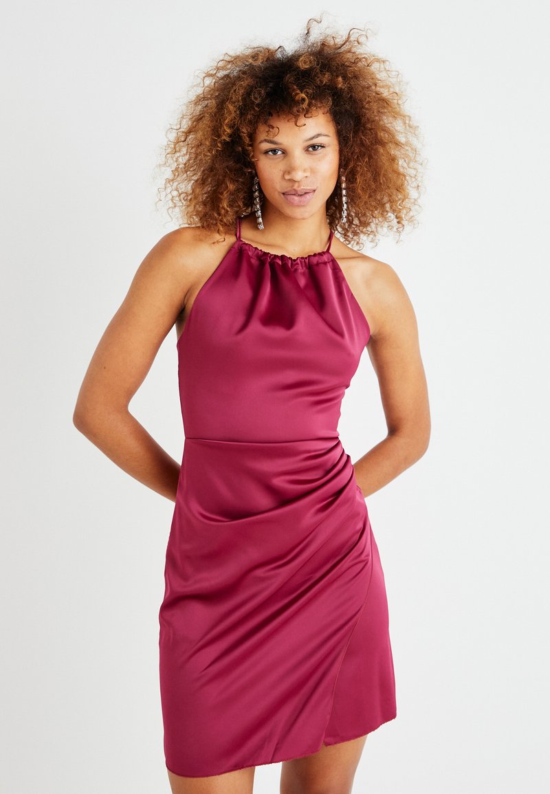 Robe en satin framboise avec un col halter et des détails froncés. Présente une silhouette ajustée avec un tissu drapé et une longueur de genou.
