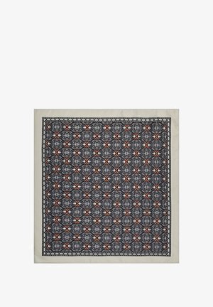 Kwadratowy jedwabny szalik z szczegółowym czarno-białym geometrycznym wzorem z czerwonymi akcentami, oprawiony jasną ramką.