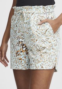 Pantaloni corti azzurri con un design a fantasia che presenta dettagli in arancione, nero e crema. Vita elastica con cordino e tasche laterali.