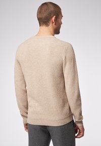 Beige gerippter Strickpullover mit langen Ärmeln, Rundhalsausschnitt und lockerer Passform. Die Stoffstruktur wirkt weich und leicht dehnbar.