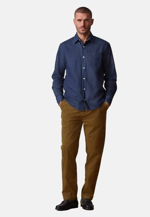 Dunkelblaues Jeanshemd mit Brusttasche und Knopfleiste; kombiniert mit braunen Chinos und schwarzen Schuhen.