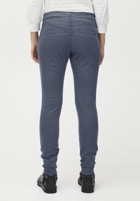 Vaqueros ajustados y elásticos en denim azul oscuro con dos bolsillos traseros, textura suave y diseño hasta el tobillo, combinados con botas negras.