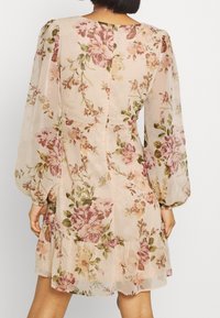 Vestido floral en tejido ligero y transparente con fondo en rosa pastel. Presenta mangas largas y abullonadas, y un dobladillo con volantes. Estampado floral en rosa y verde.