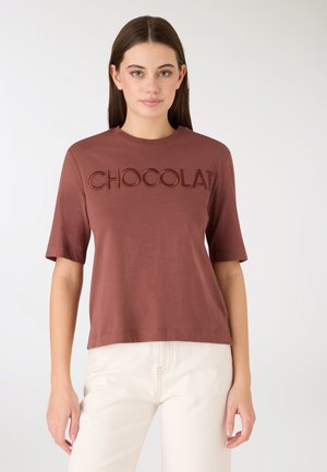 T-shirt di cotone marrone con la scritta "CHOCOLAT" ricamata con filo dello stesso colore. Maniche corte, scollo rotondo, vestibilità comoda, tessuto liscio.