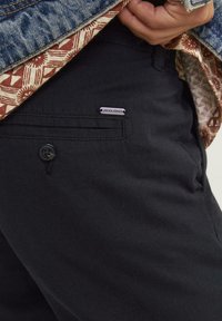 Melnas kokvilnas bikses ar priekšējo pogu aizdari, sānu kabatu un "JACK & JONES" logo uzlīmi kreisajā pusē.