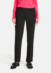 Schwarze gerade geschnittene Hose aus einem glatten, strukturierten Stoff. Mit einem Knopfverschluss und vorderen Taschen. Kombiniert mit schwarzen Schuhen.