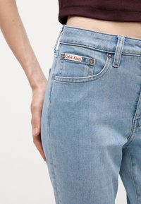 Svetlo modré denimové nohavice s priliehavým strihom, s viditeľnou etikou Calvin Klein, prednými vreckami a striebornými akcentmi.