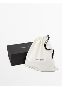 Cotton drawstring bag in white with “Massimo Dutti” printed in black, next to a sleek black box with the same brand name embossed on it.