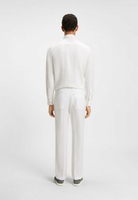 White long-sleeve shirt and matching trousers made of lightweight fabric. The outfit features a smooth texture and straight-leg silhouette.