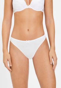 Witte katoenen string met een gladde textuur, voorzien van een klein strikje aan de voorkant en een minimalistisch ontwerp.