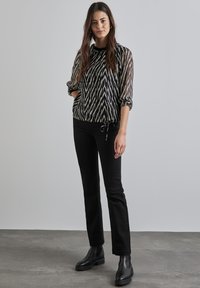 Blusa trasparente a righe zigzag bianche e nere con orlo a cordoncino e maniche elasticizzate, abbinata a jeans neri slim-fit e stivaletti alla caviglia.