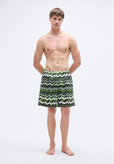 Ανδρικό μαγιό σε ζιγκ ζαγκ μοτίβο πράσινου και μαύρου, κατασκευασμένο από ελαφρύ ύφασμα με ελαστική μέση και κορδόνι.