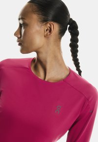 Užitak dugih rukava u jarkoj ružičastoj boji, teksturiranom materijalu, okruglom izrezu, sa logotipom na prsima i bešavnim dizajnom ramena.