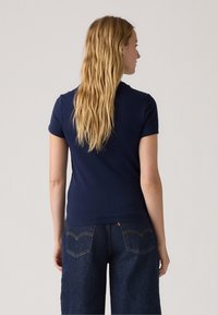 T-shirt en coton bleu marine à manches courtes, au design ajusté et avec un col rond, porté avec un jean en denim foncé taille haute.