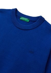 Modrý svetr s kulatým výstřihem a žebrovaným límcem, s jemně vyšitým logem na hrudi a zelenou nálepku "United Colors of Benetton" uvnitř výstřihu.