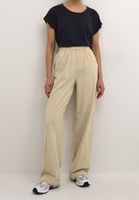 Beige vida byxor med elasticitet i midjan, ihop med en mörk kortärmad topp. Vita och grå sportskor fulländar outfiten.