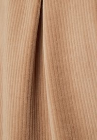 Beiger Cordstoff mit vertikalen Rippen, der eine weiche Textur und einen dezenten Glanz aufweist und in Falten drapiert ist, um zusätzliche Dimension zu verleihen.