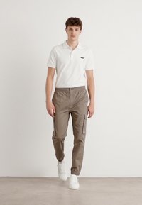 Męski zestaw składający się z białej koszulki polo oraz brązowych spodni cargo z elastycznymi mankietami i kieszeniami bocznymi, w połączeniu z białymi sneakersami.